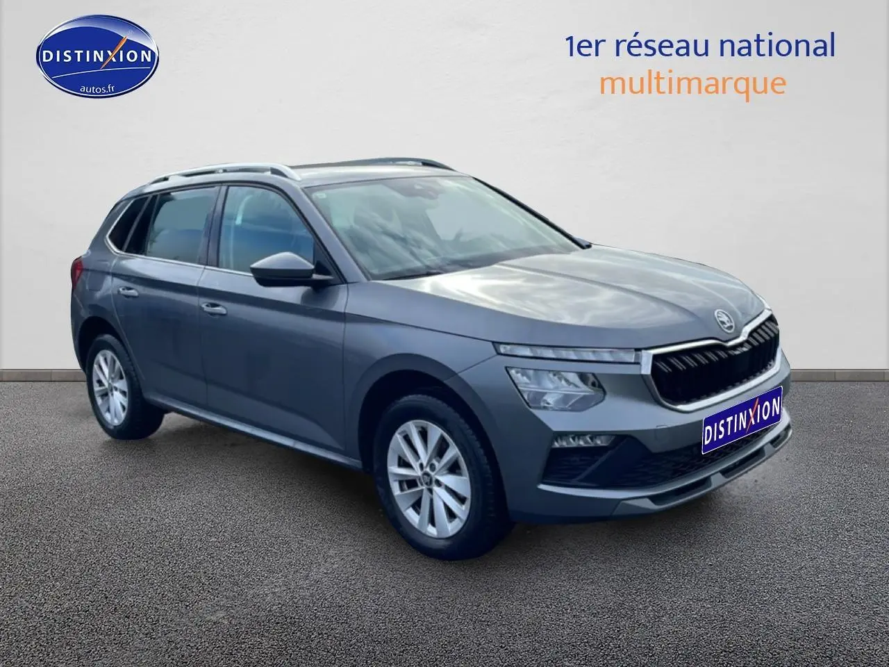 SUV Skoda Kamiq gris en 3/4 avant droit avec calandre chromée et barres de toit visibles.