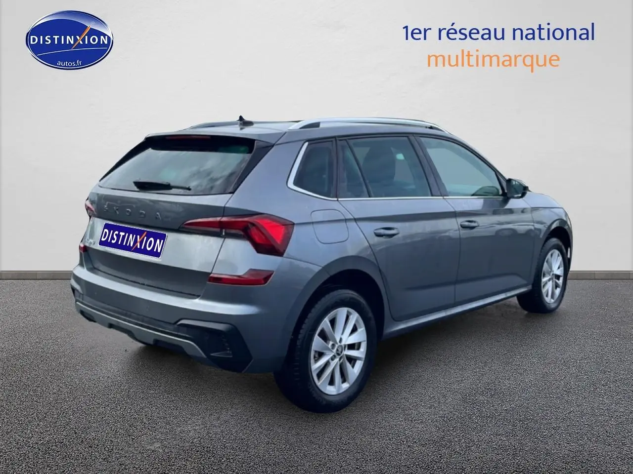 Vue 3/4 arrière droite d'un Skoda Kamiq gris avec barres de toit et jantes alu sur fond neutre.