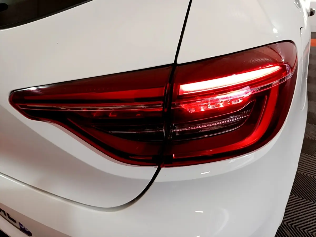 Gros plan sur le feu arrière droit rouge d'une Renault Clio Business blanche, soulignant la carrosserie lisse et brillante.