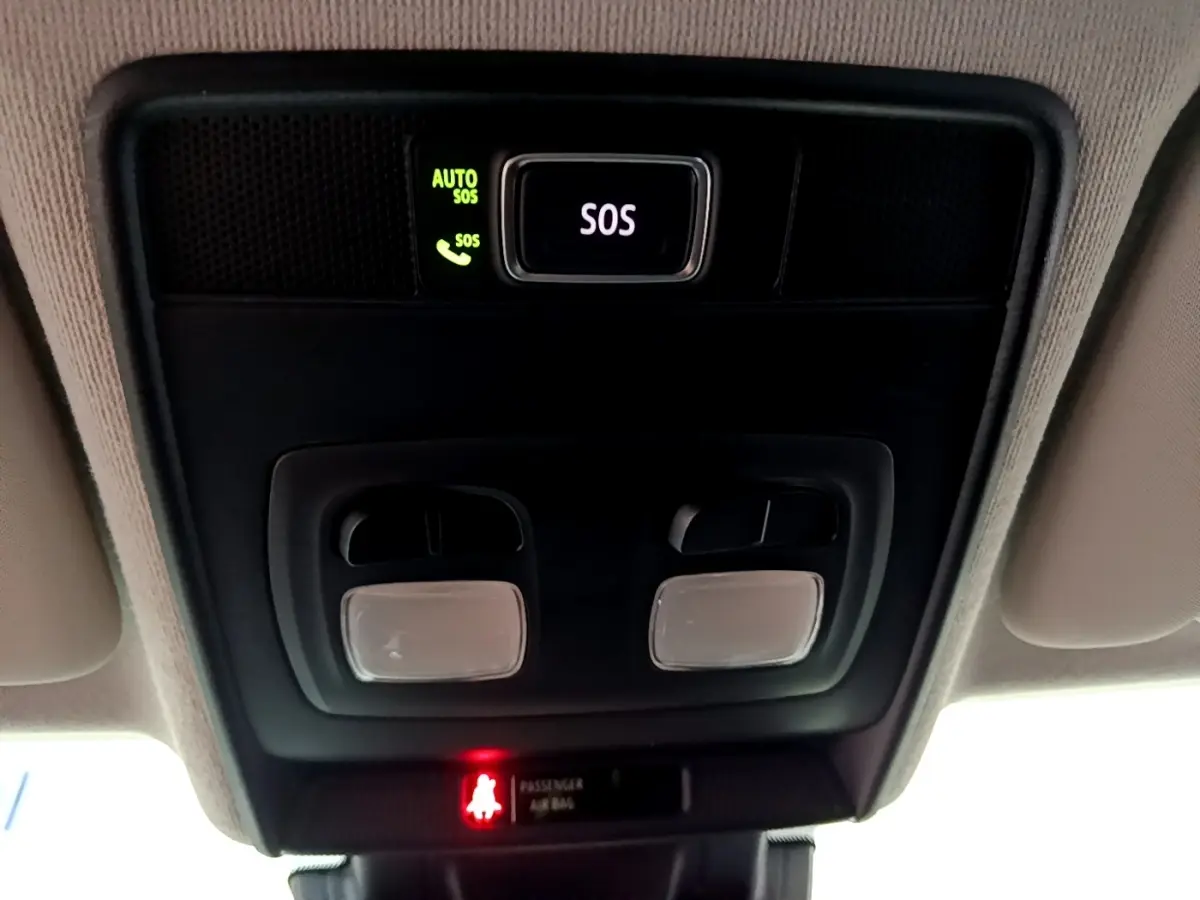 Vue en gros plan du plafonnier intérieur noir avec bouton SOS éclairé en vert et lampes de lecture dans une Renault Clio blanche.