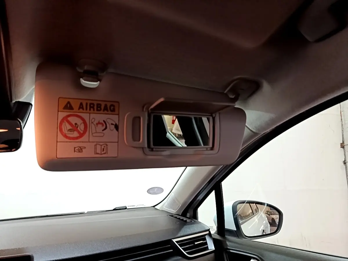 Intérieur de la Renault Clio Business blanche, vue côté passager avec pare-soleil et miroir de courtoisie ouverts.
