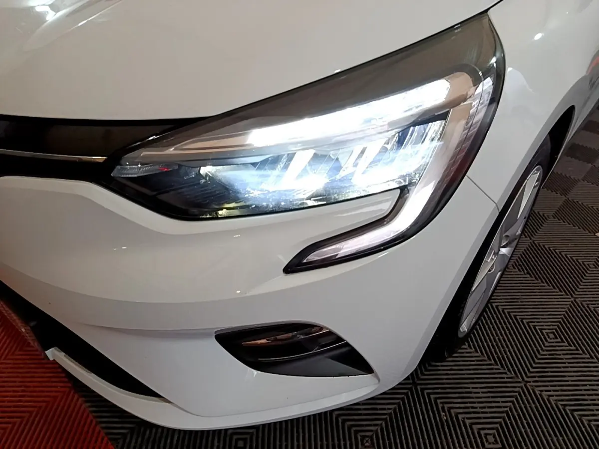 Gros plan sur l'avant droit blanc d'une Renault Clio 2021 avec phares LED allumés et jante visible.