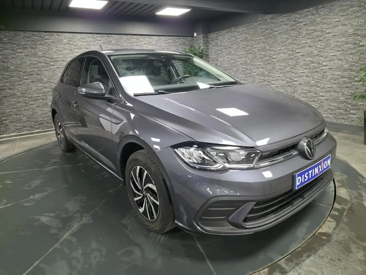 Volkswagen Polo gris métallisé vue 3/4 avant droit en intérieur avec jantes alliage et calandre chromée.