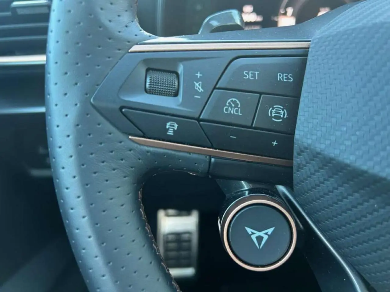 Gros plan sur le volant perforé du CUPRA Formentor blanc 2025, avec commandes intégrées et logo distinctif au centre.