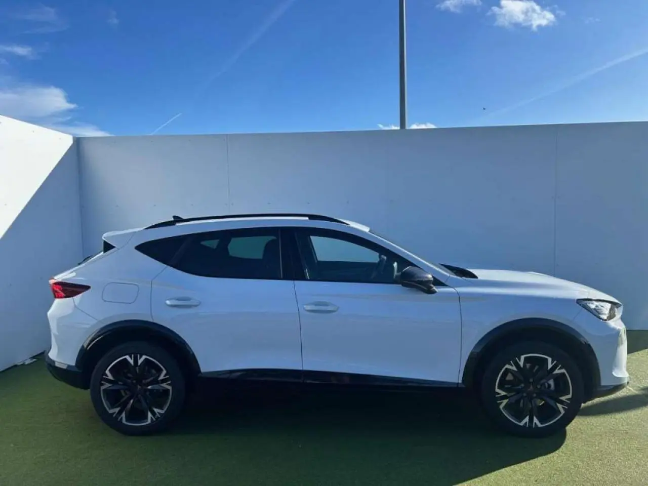 Vue de profil côté gauche d'un CUPRA Formentor blanc 2025 avec jantes noires et toit ouvrant, stationné en extérieur.