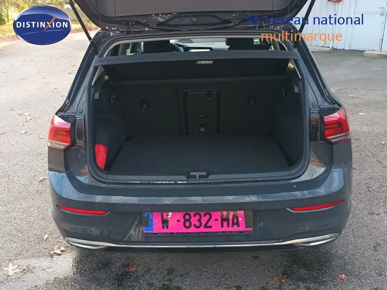 Vue arrière d'une Volkswagen Golf gris Urano 2024 avec coffre ouvert sur un parking extérieur.