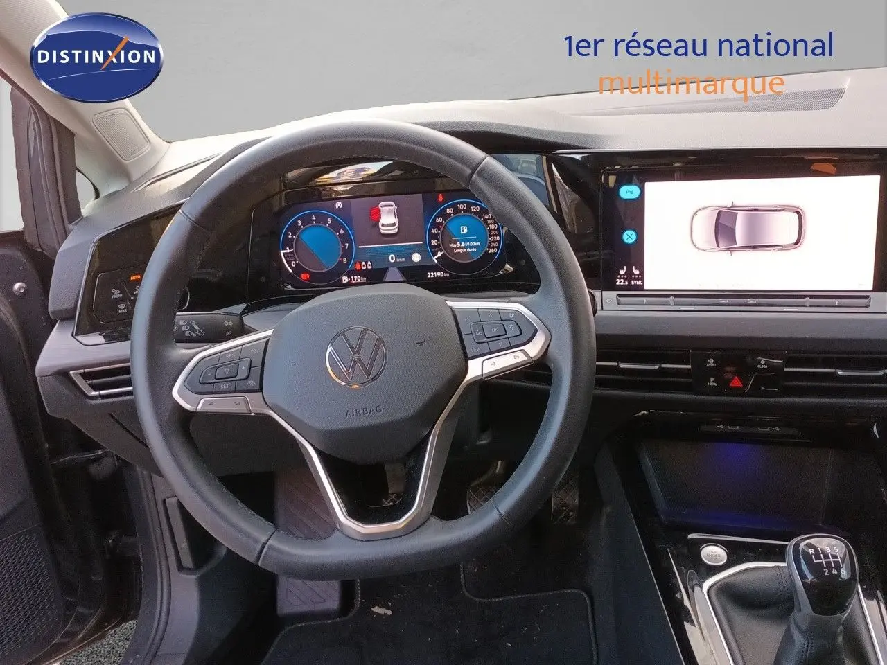 Vue intérieure centrée sur le volant et tableau de bord numérique d’une Volkswagen Golf gris Urano avec boîte manuelle.