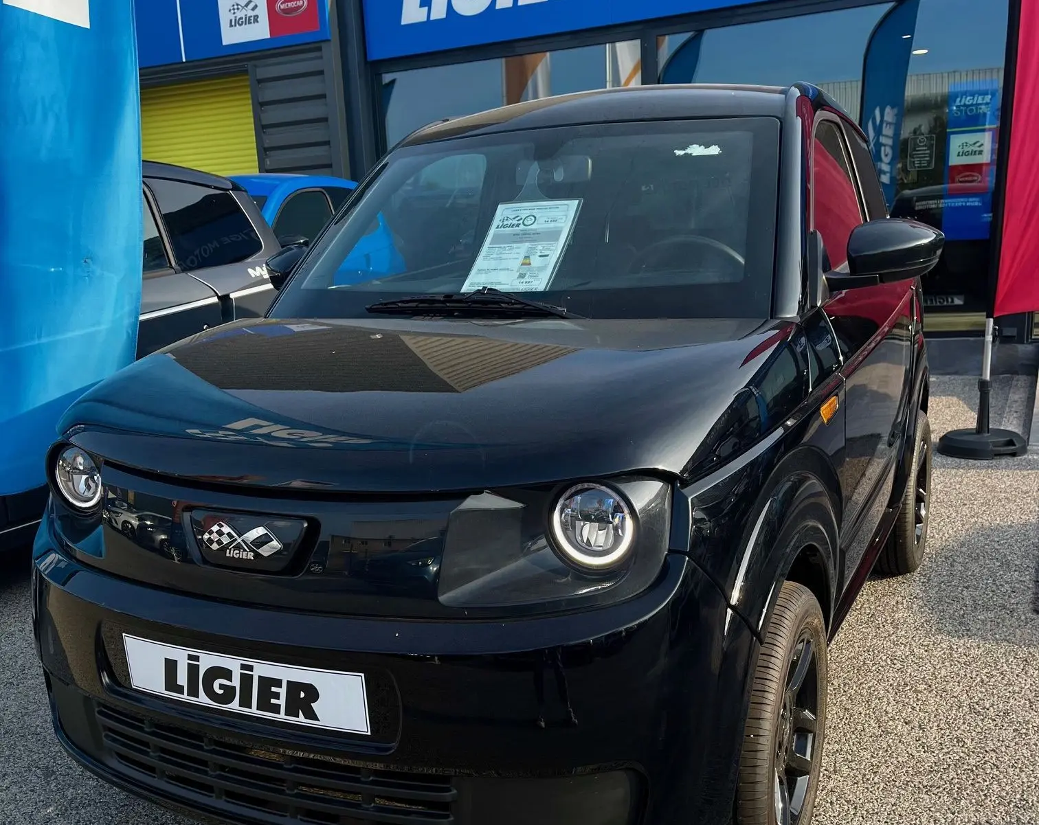 Vue 3/4 avant d'une Ligier Myli I.DEL 8KWH noire intense électrique, devant un magasin Ligier Store.