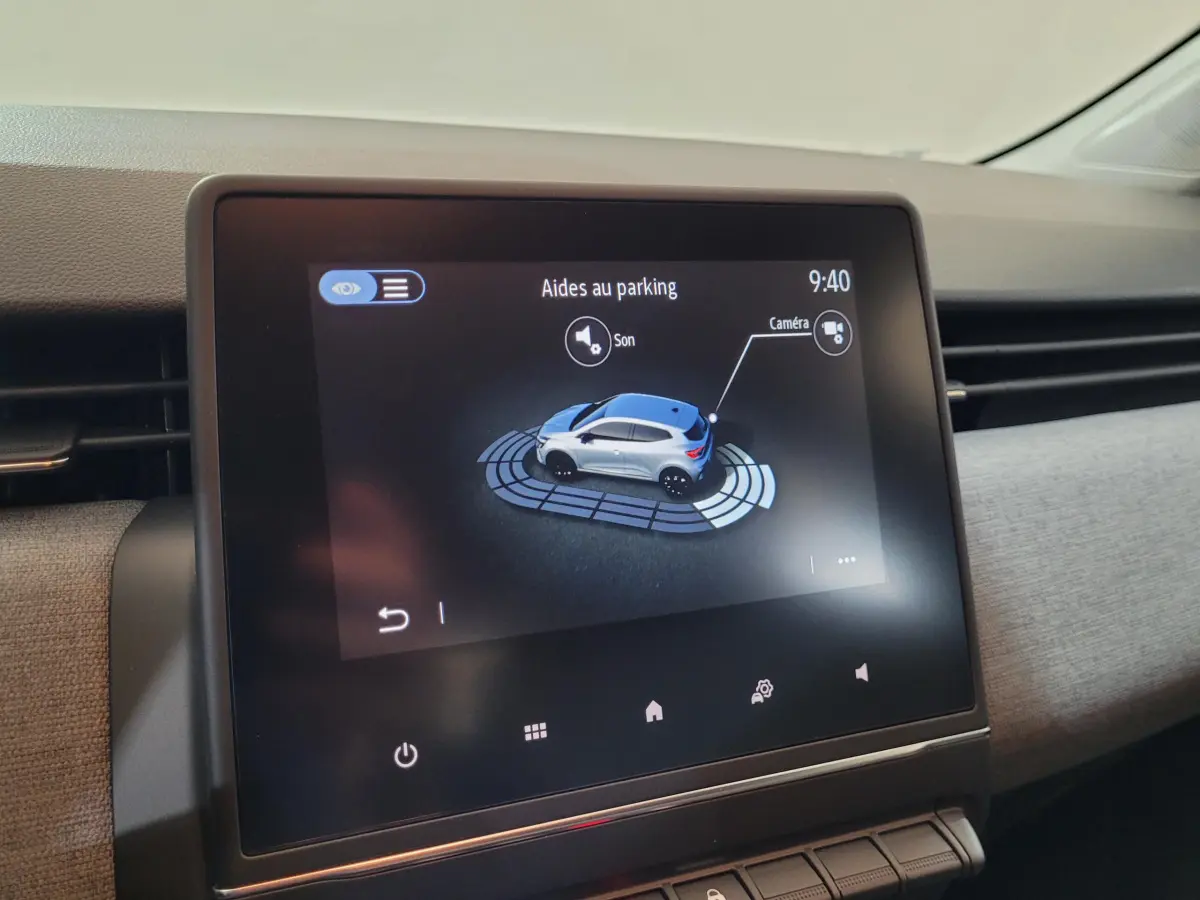 Écran tactile intérieur montrant l'aide au parking avec vue 3D d'une Renault Clio bleue, tableau de bord moderne.