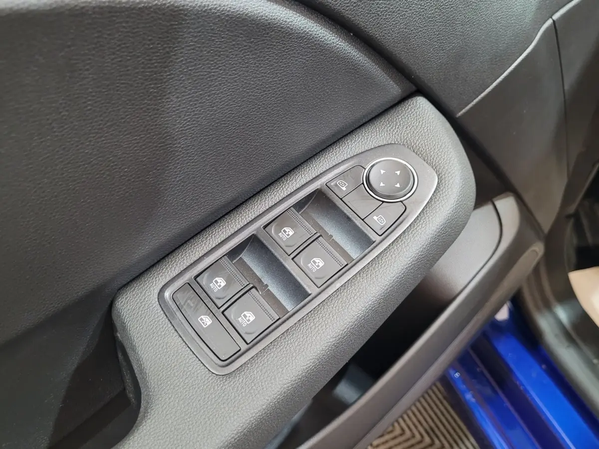 Gros plan sur les commandes des vitres électriques côté conducteur d’une Renault Clio bleu Evolution 2025.