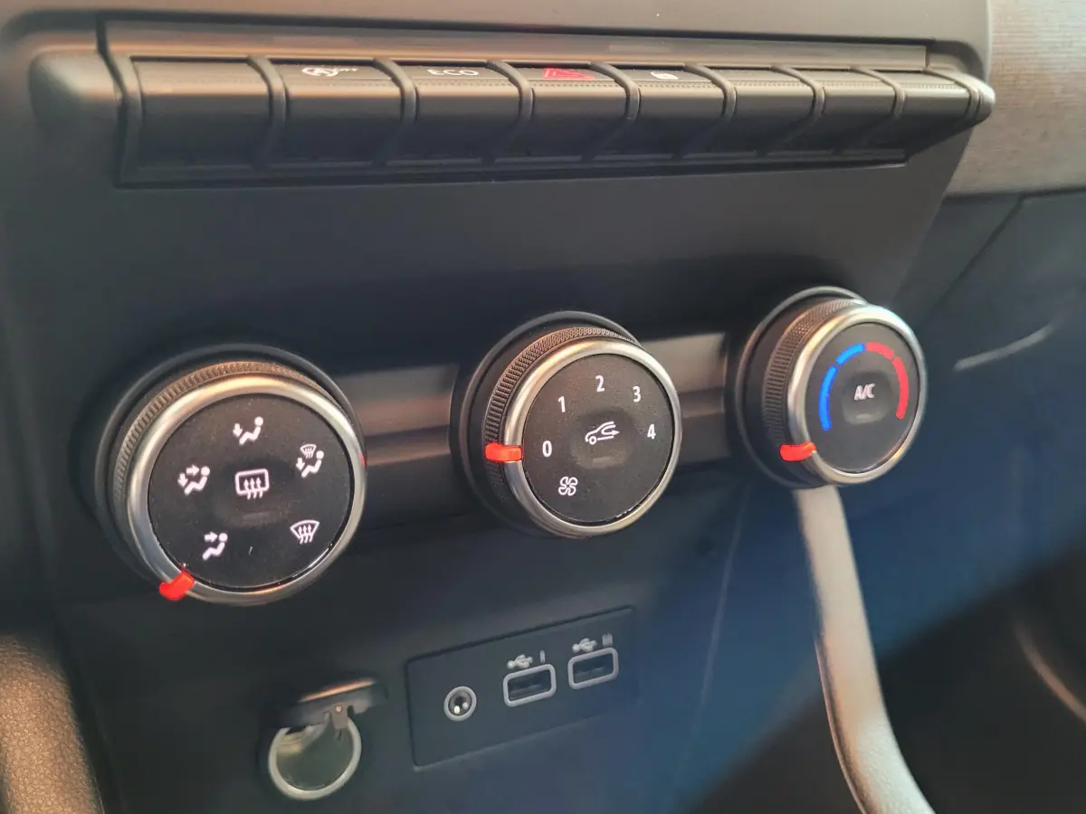Gros plan sur les commandes de climatisation et les ports USB du tableau de bord de la Renault Clio bleu.