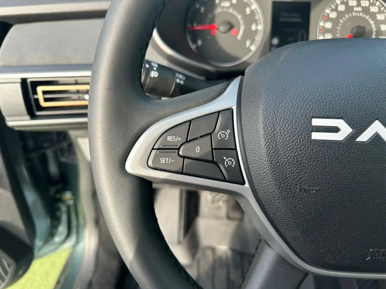 Gros plan sur le volant noir de la Dacia Sandero III Stepway, montrant les commandes de régulateur de vitesse côté gauche.