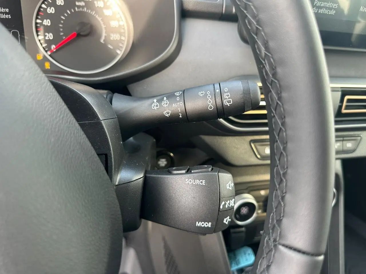 Gros plan sur la commande au volant côté gauche d'une Dacia Sandero III Stepway, intérieur noir avec tableau de bord numérique.