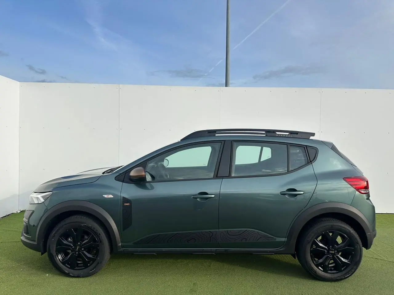 Profil droit de la Dacia Sandero III Stepway 2025 vert cèdre avec jantes noires et détails brun cuivré.