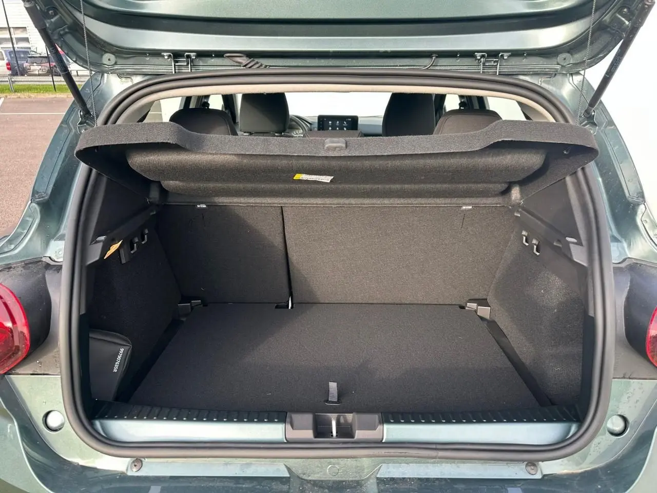 Coffre ouvert vu de l'arrière d'une Dacia Sandero III Stepway vert cèdre avec cache-bagages relevé.