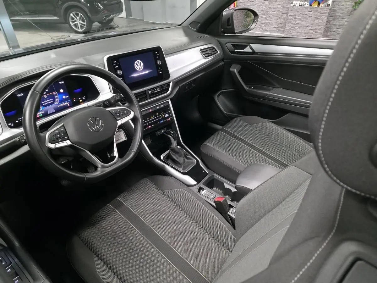 Vue intérieure côté conducteur du Volkswagen T-Roc Cabriolet 2024, sellerie tissu noire et tableau de bord moderne.