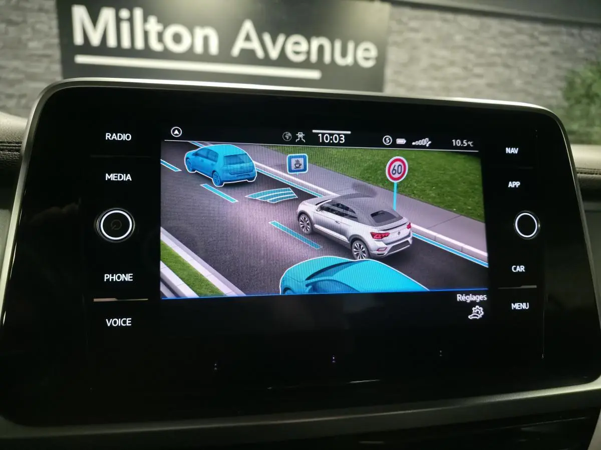 Écran central affichant une simulation 3D du Volkswagen T-Roc gris vu de l'arrière droit avec signalisation routière.
