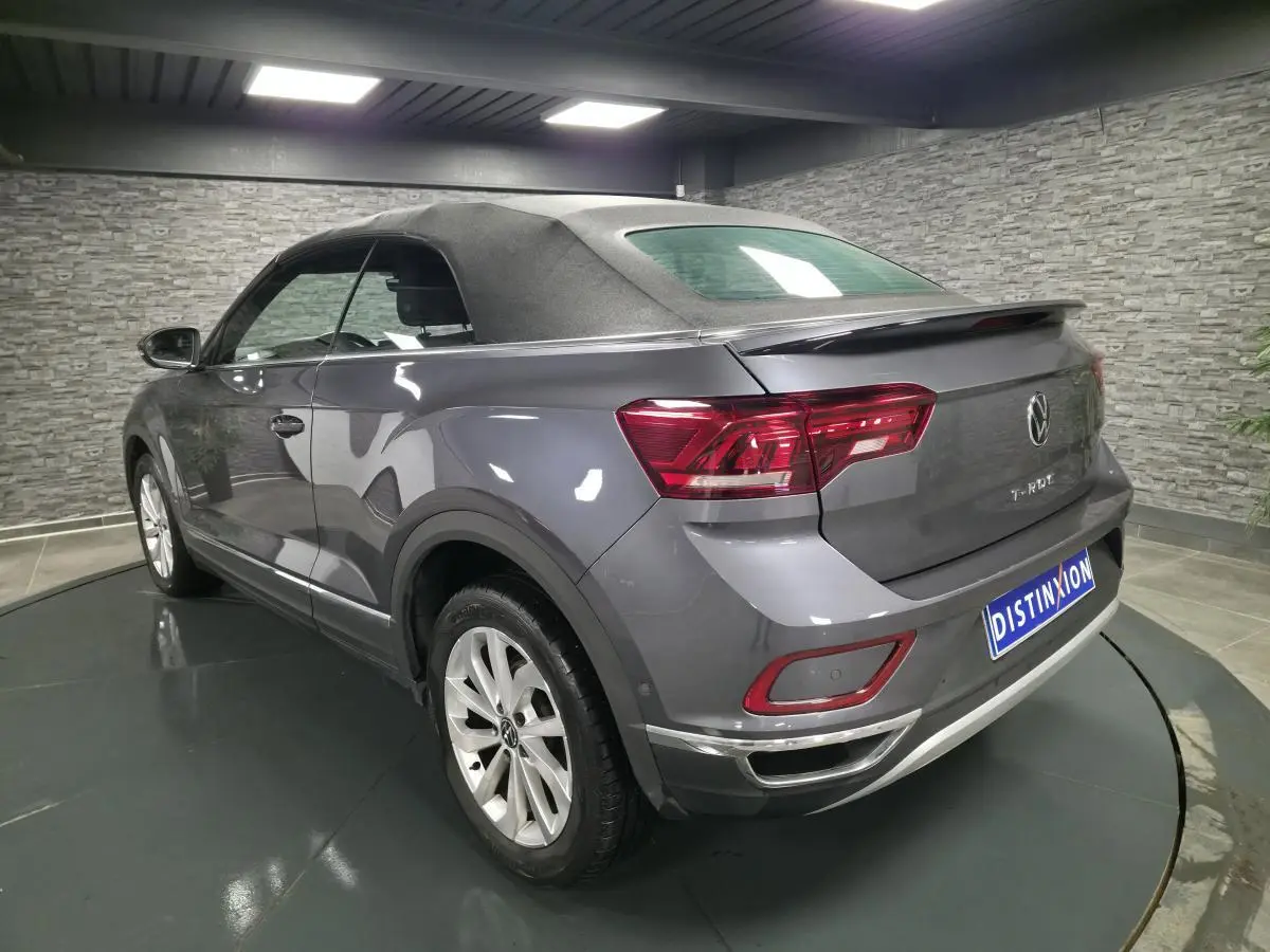 Vue 3/4 arrière droite du Volkswagen T-Roc Cabriolet gris métallisé avec capote noire en intérieur showroom.