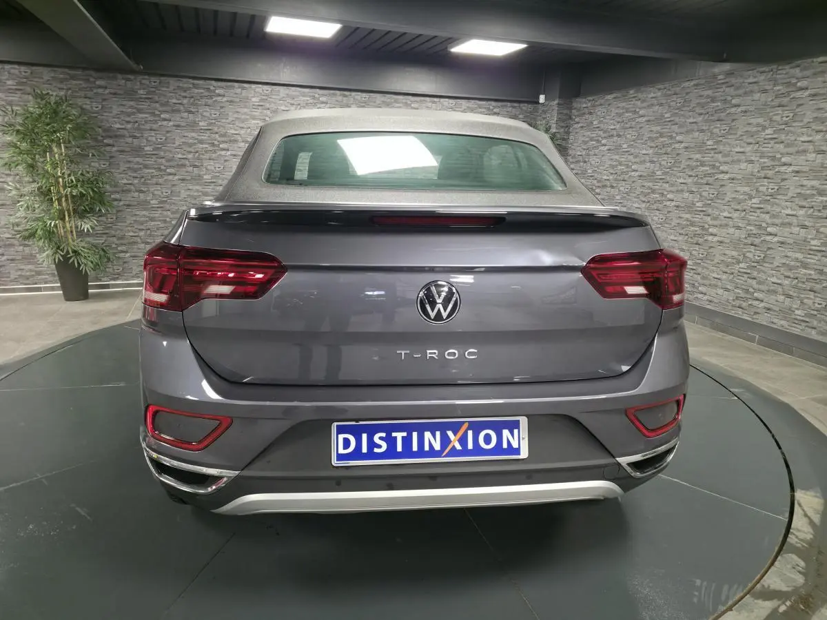 Vue arrière d'un Volkswagen T-Roc Cabriolet gris métallisé 2024 avec capote textile noire et feux arrière LED.