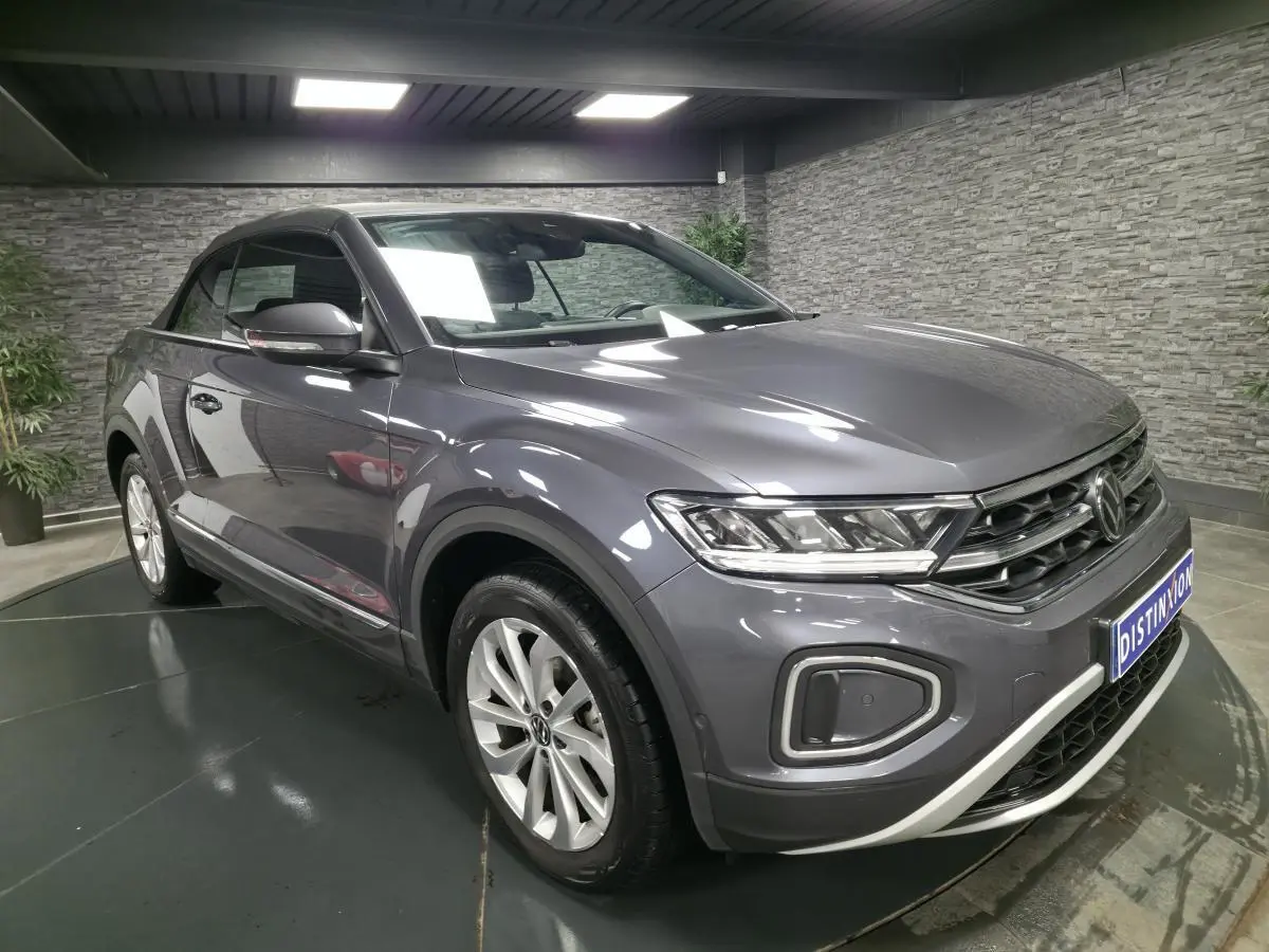 Volkswagen T-Roc cabriolet gris métallisé en 3/4 avant droit dans un showroom avec capote noire fermée.
