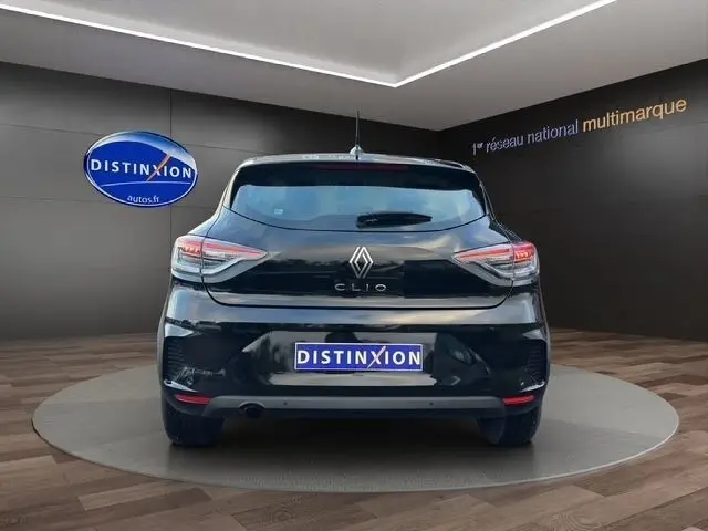 Vue arrière d'une Renault Clio noire 2025, avec feux LED et logo distinctif sur fond de showroom multimarque.