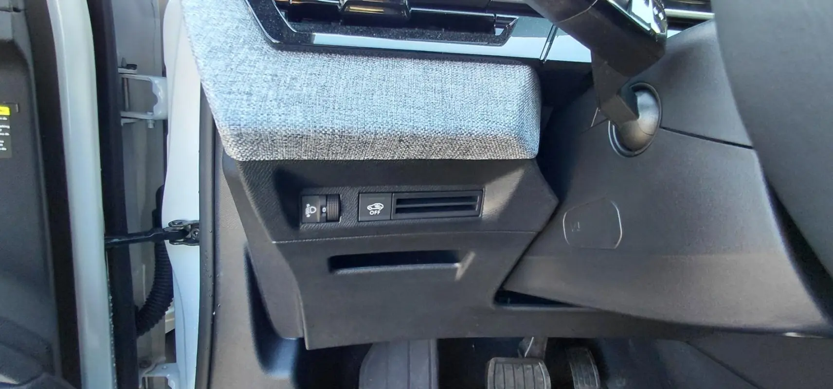 Détail de la console côté gauche sous le tableau de bord du Peugeot 5008 blanc Hybrid 2025 avec commandes et tissu gris.