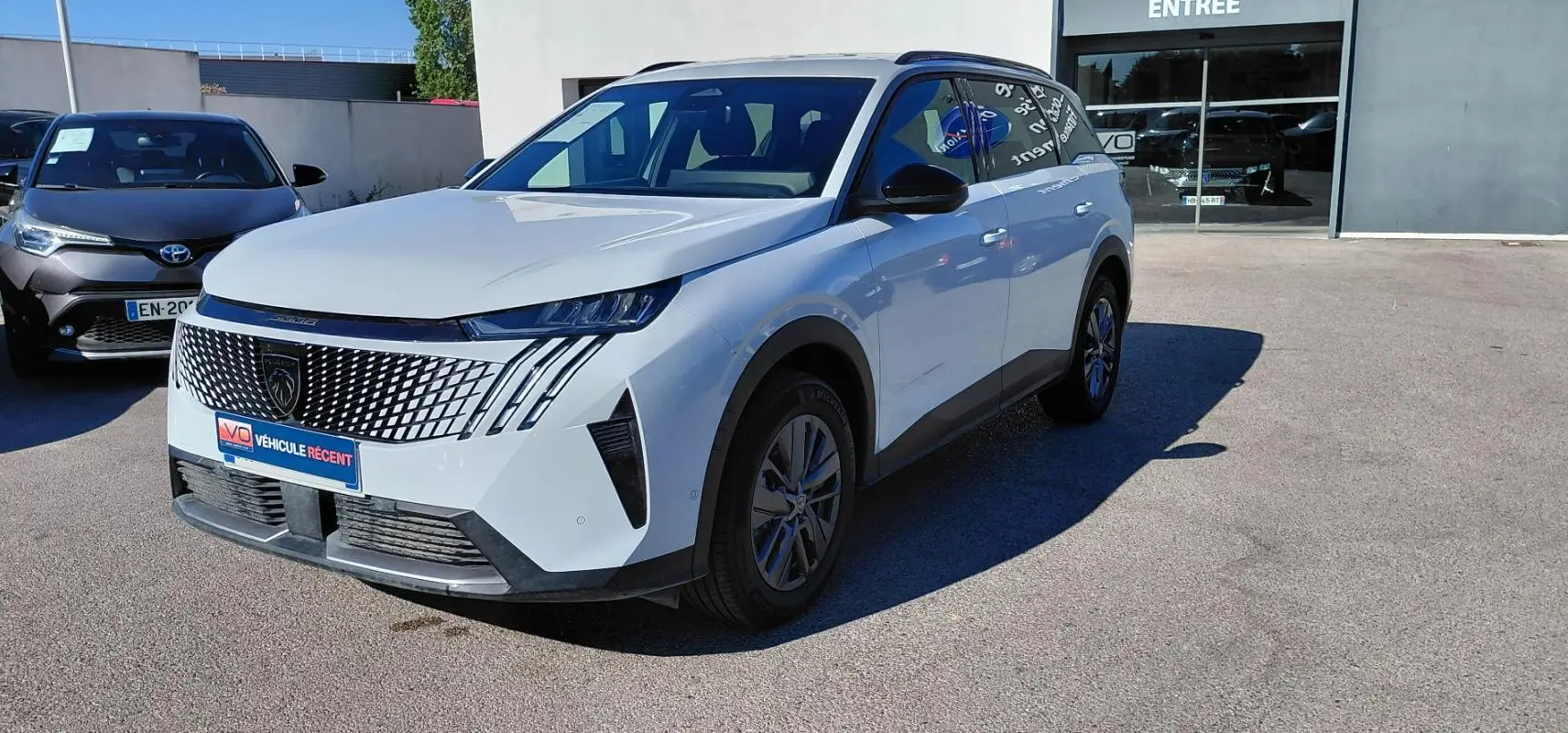 Peugeot 5008 Hybrid blanc vue 3/4 avant droit, avec calandre distinctive et feux LED verticaux.