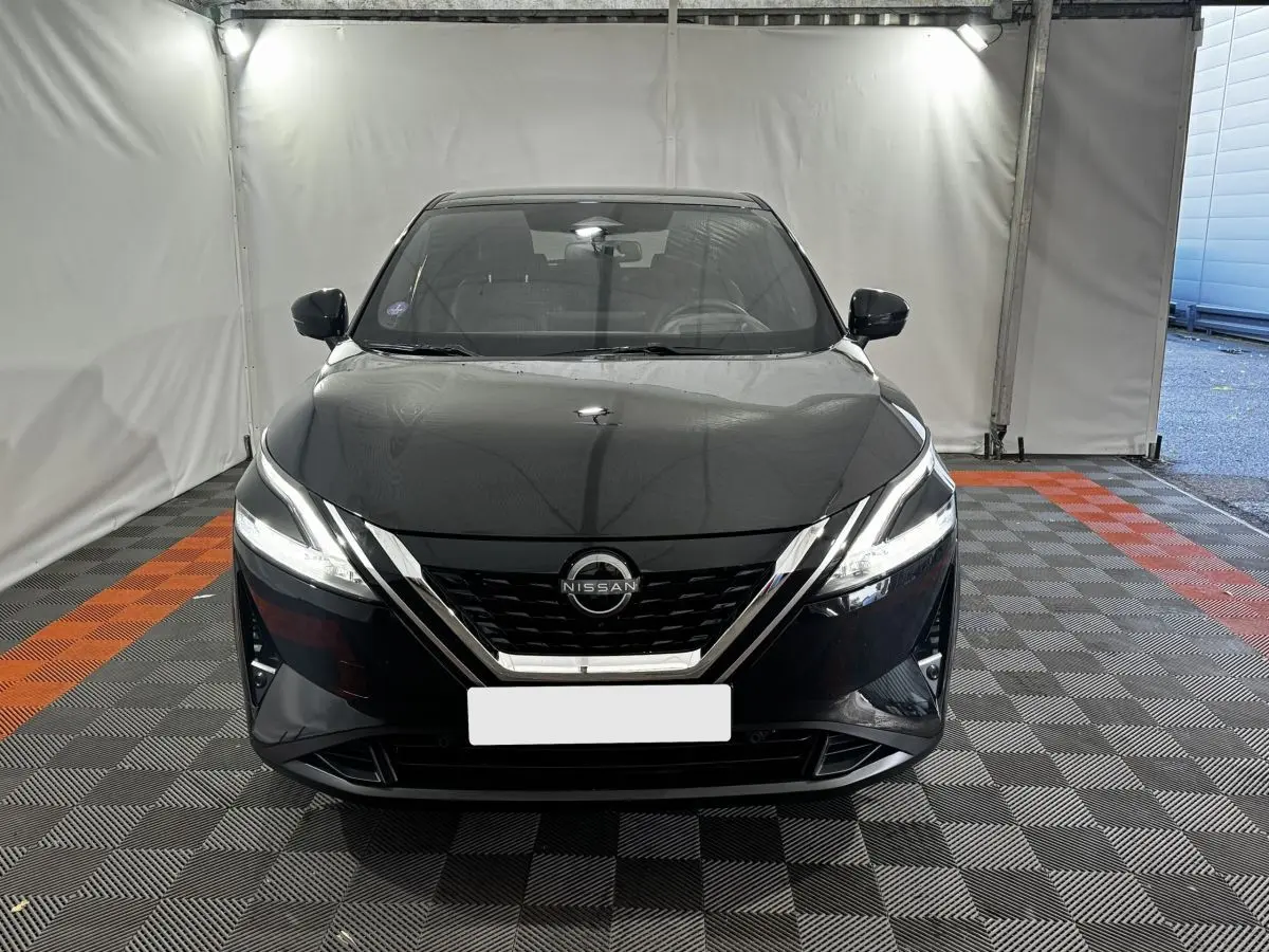 Vue avant d'un Nissan Qashqai e-Power 190 Tekna BVA noir avec phares LED et calandre chromée dans un garage.