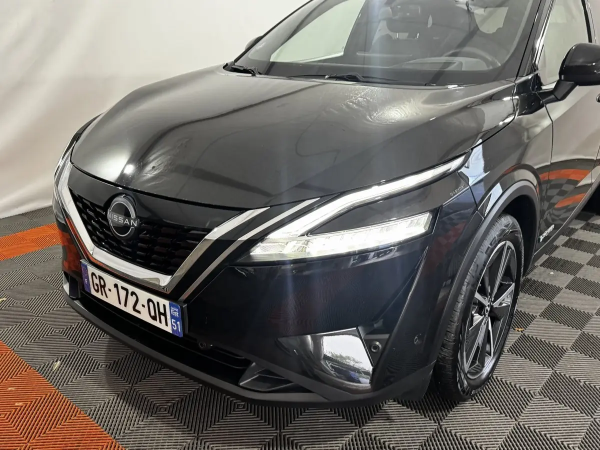 Vue 3/4 avant droit du Nissan Qashqai e-Power noir, avec calandre V-motion et phares LED allumés.