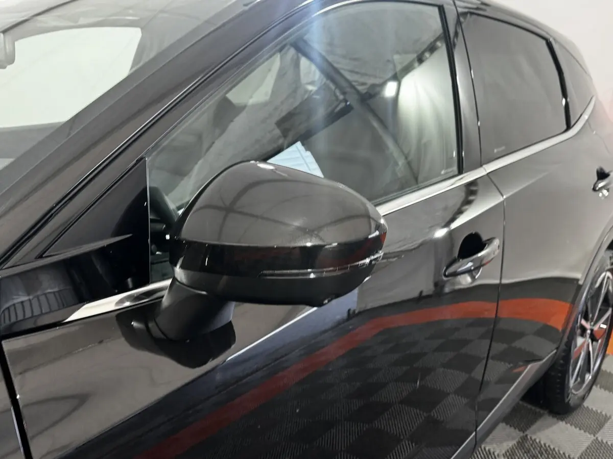 Vue rapprochée du rétroviseur côté gauche d’un Nissan Qashqai e-Power noir brillant avec porte et jante partiellement visibles.