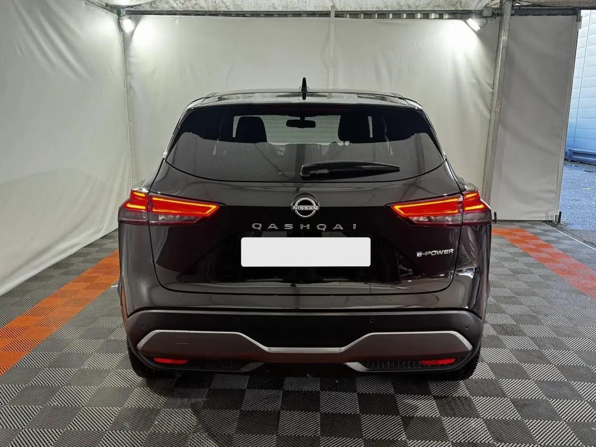 Vue arrière d'un Nissan Qashqai e-Power noir avec feux LED allumés dans un espace intérieur éclairé.