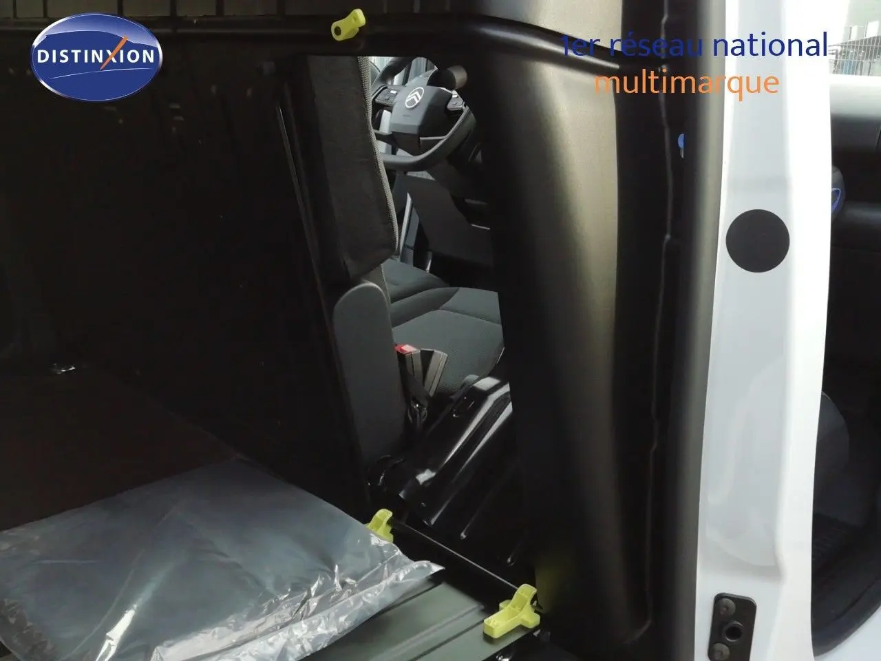 Vue intérieure depuis la porte latérale droite ouverte d'un Citroën Berlingo XL blanc, montrant les sièges avant et arrière en tissu gris.