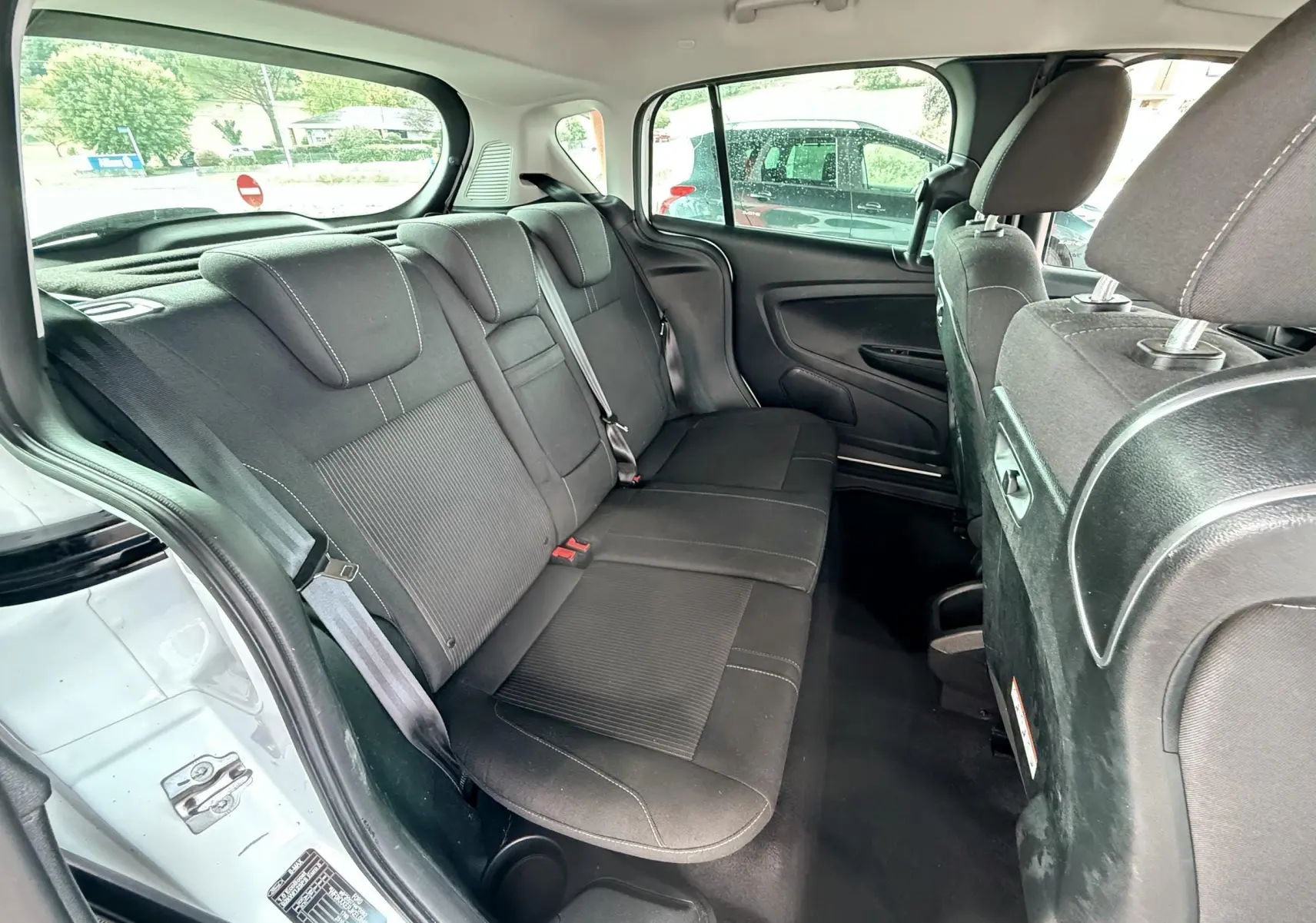 Vue intérieure arrière du Ford B-MAX blanc de 2014, montrant les sièges arrière en tissu gris noir et les ceintures de sécurité.