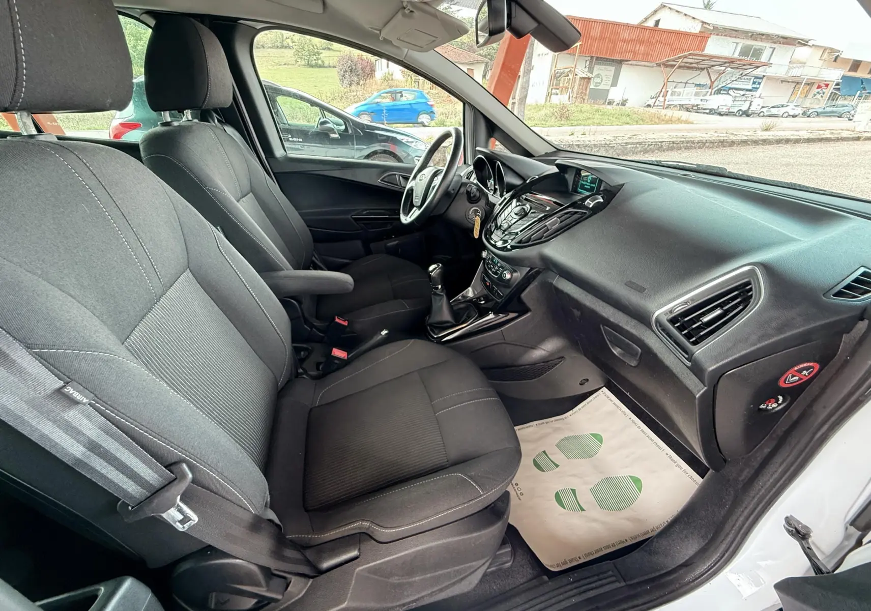 Vue intérieure côté passager du Ford B-MAX blanc de 2014, montrant les sièges tissu gris et le tableau de bord noir.