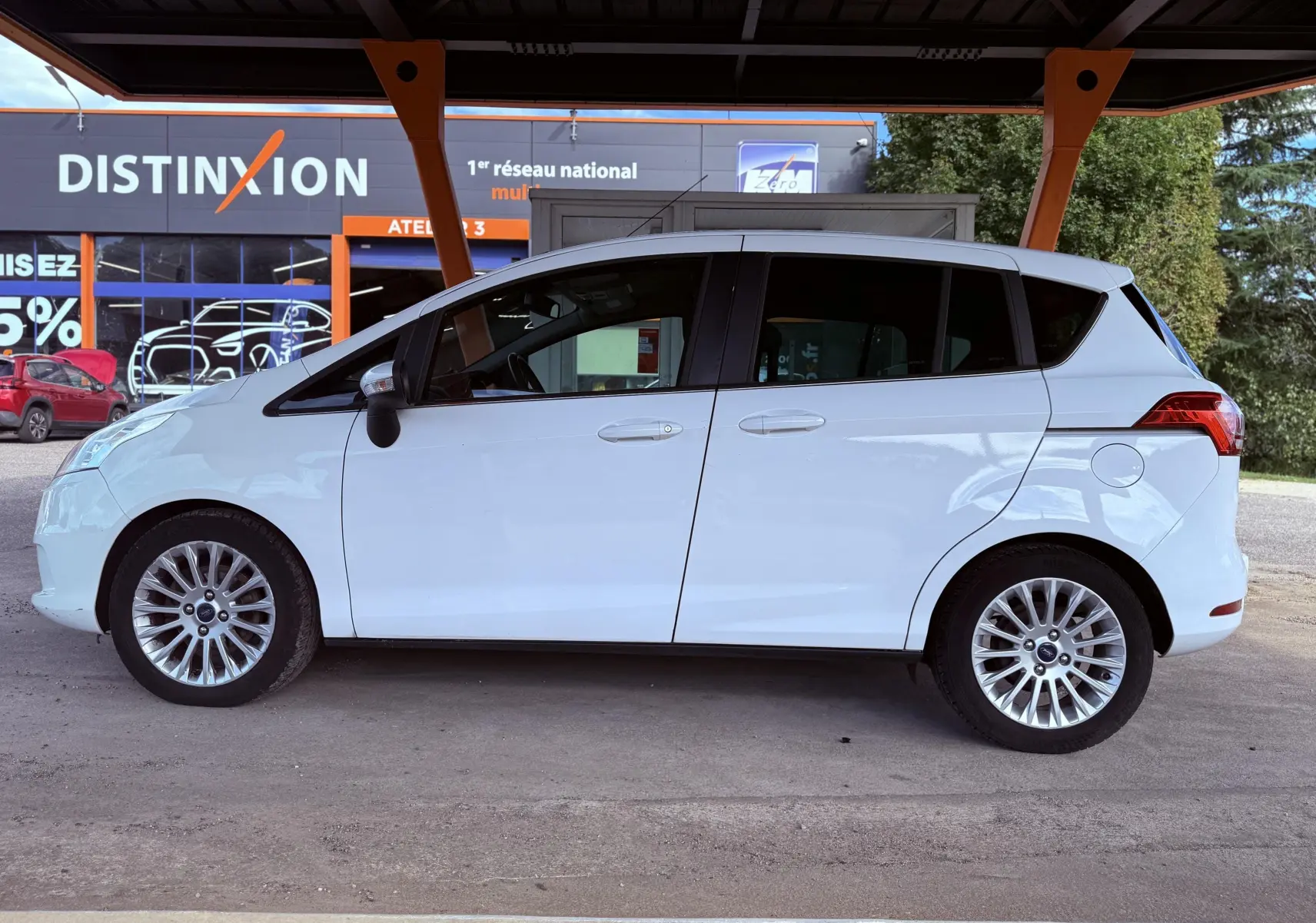 Profil côté gauche d'une Ford B-MAX blanche de 2014 avec jantes alliage et vitres teintées, stationnée sous abri.