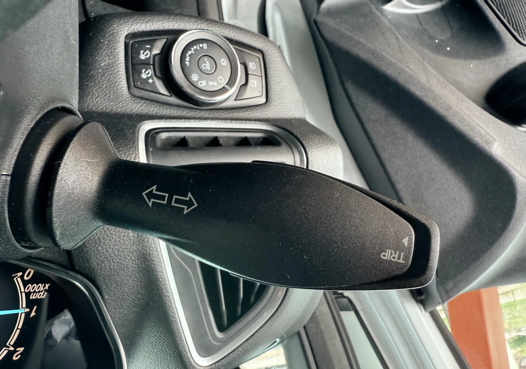 Gros plan sur la manette de clignotant noir dans l'habitacle d'une Ford B-MAX blanche, avec commandes d'éclairage en arrière-plan.