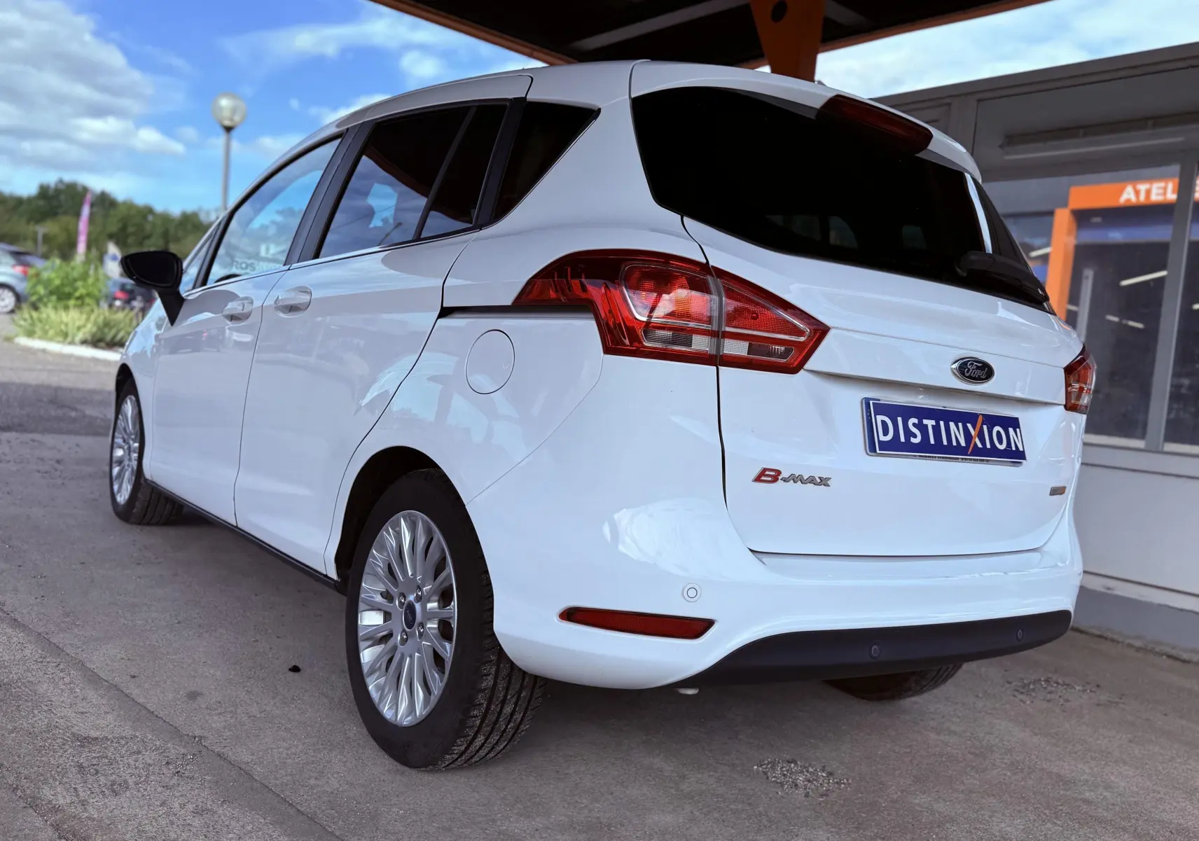 Vue 3/4 arrière gauche d'une Ford B-MAX blanche stationnée sous un abri avec jantes alliage visibles.