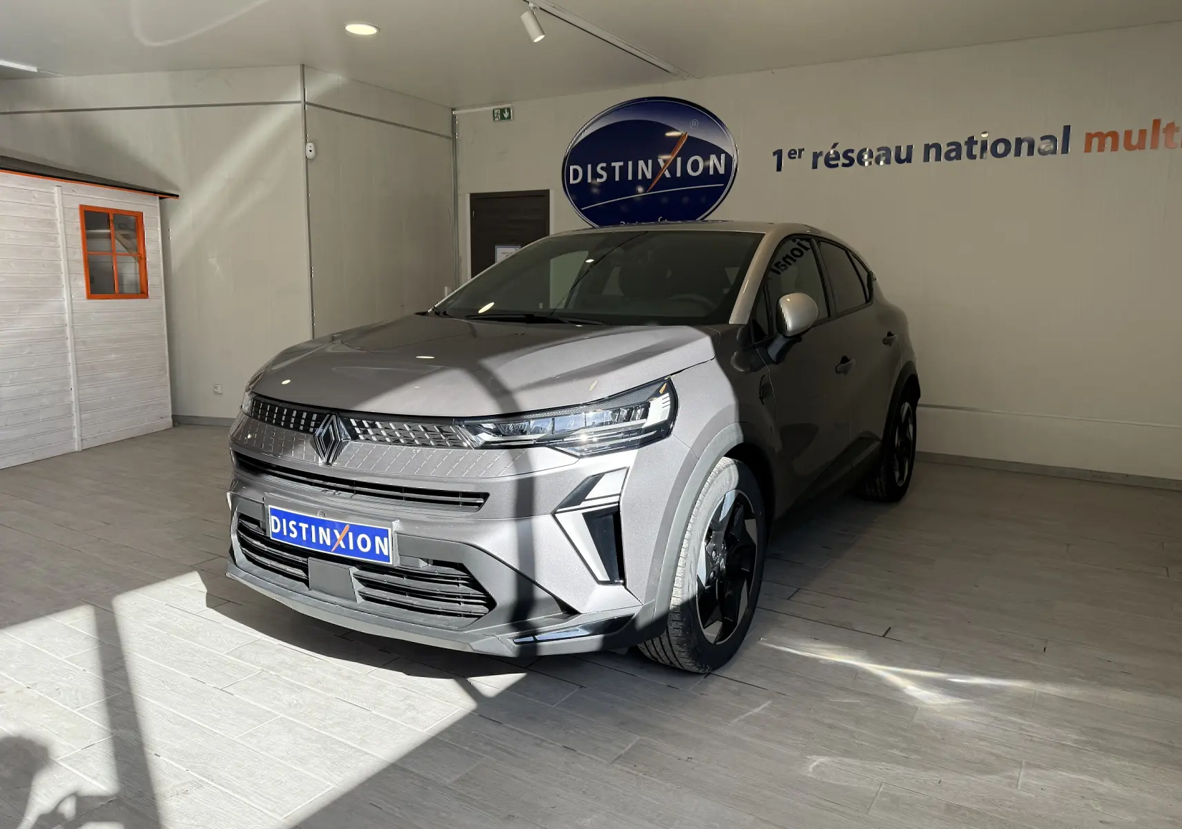 Renault Captur 2025 gris cassiopée 3/4 avant droit en showroom avec calandre moderne et jantes noires.