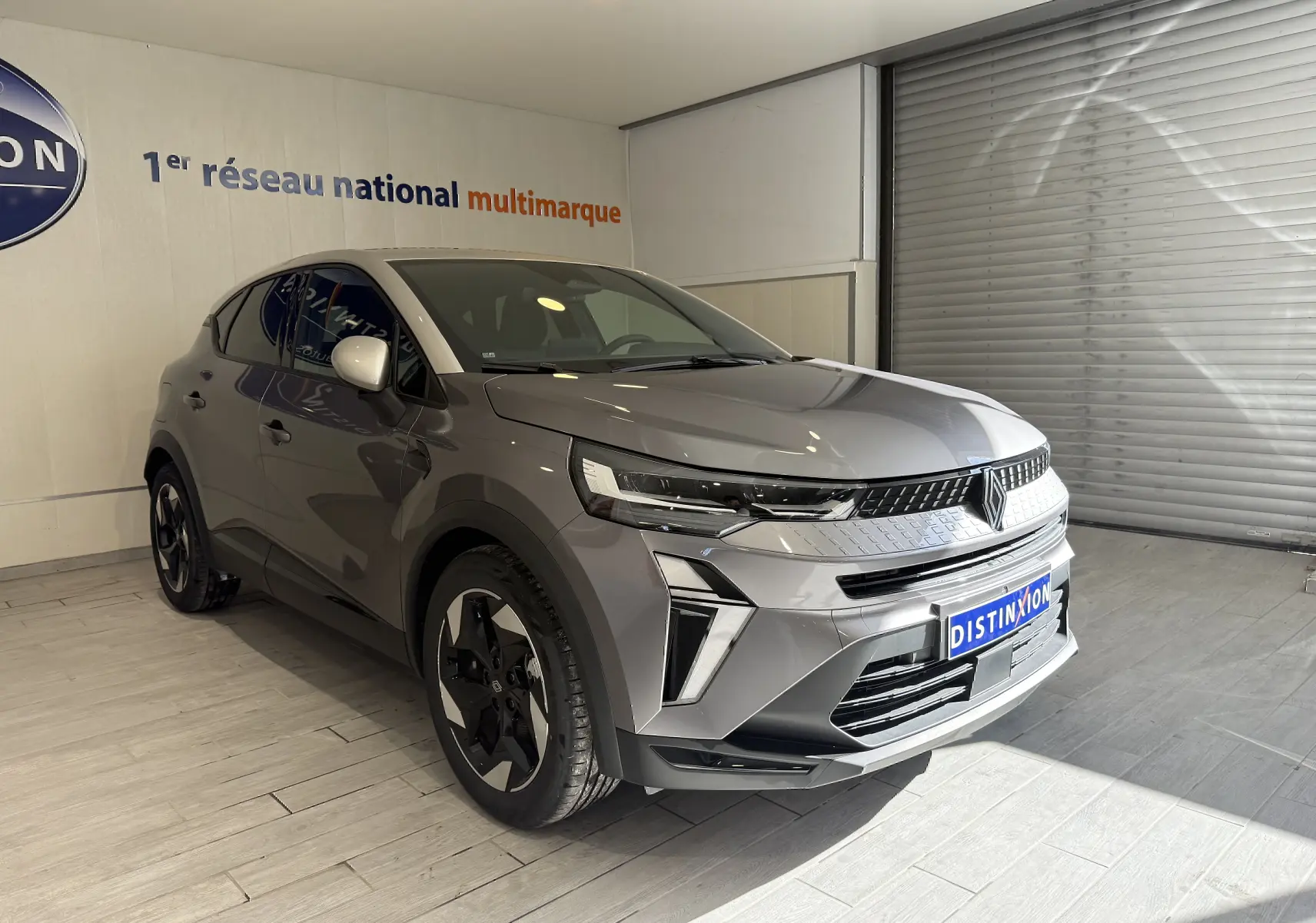 Renault Captur 2025 gris Cassiopée métal avec toit gris, vue 3/4 avant droit en intérieur showroom.