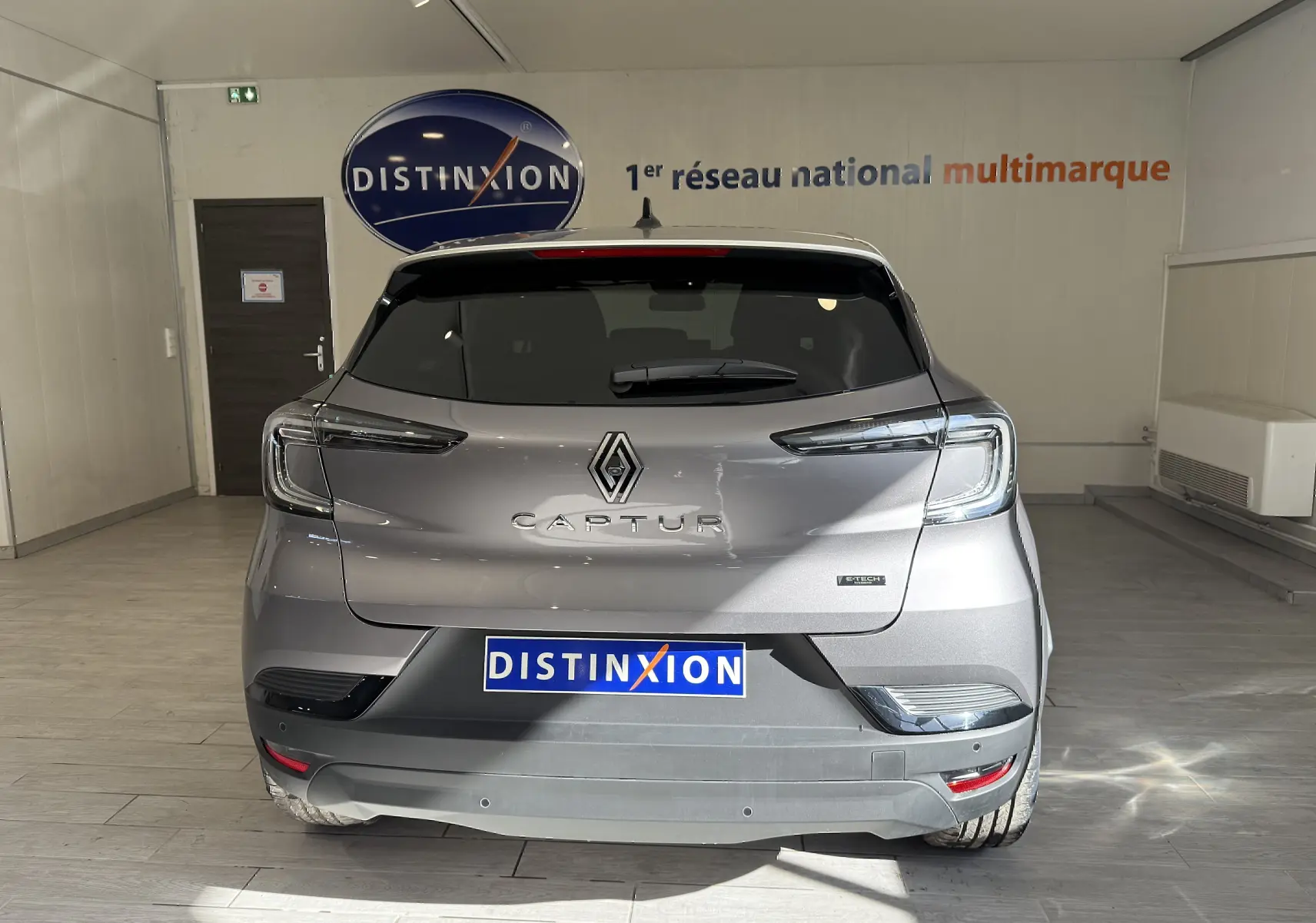 Vue arrière du Renault Captur gris Cassiopée métal avec toit gris, en intérieur, mettant en valeur ses feux LED et logo distinctif.