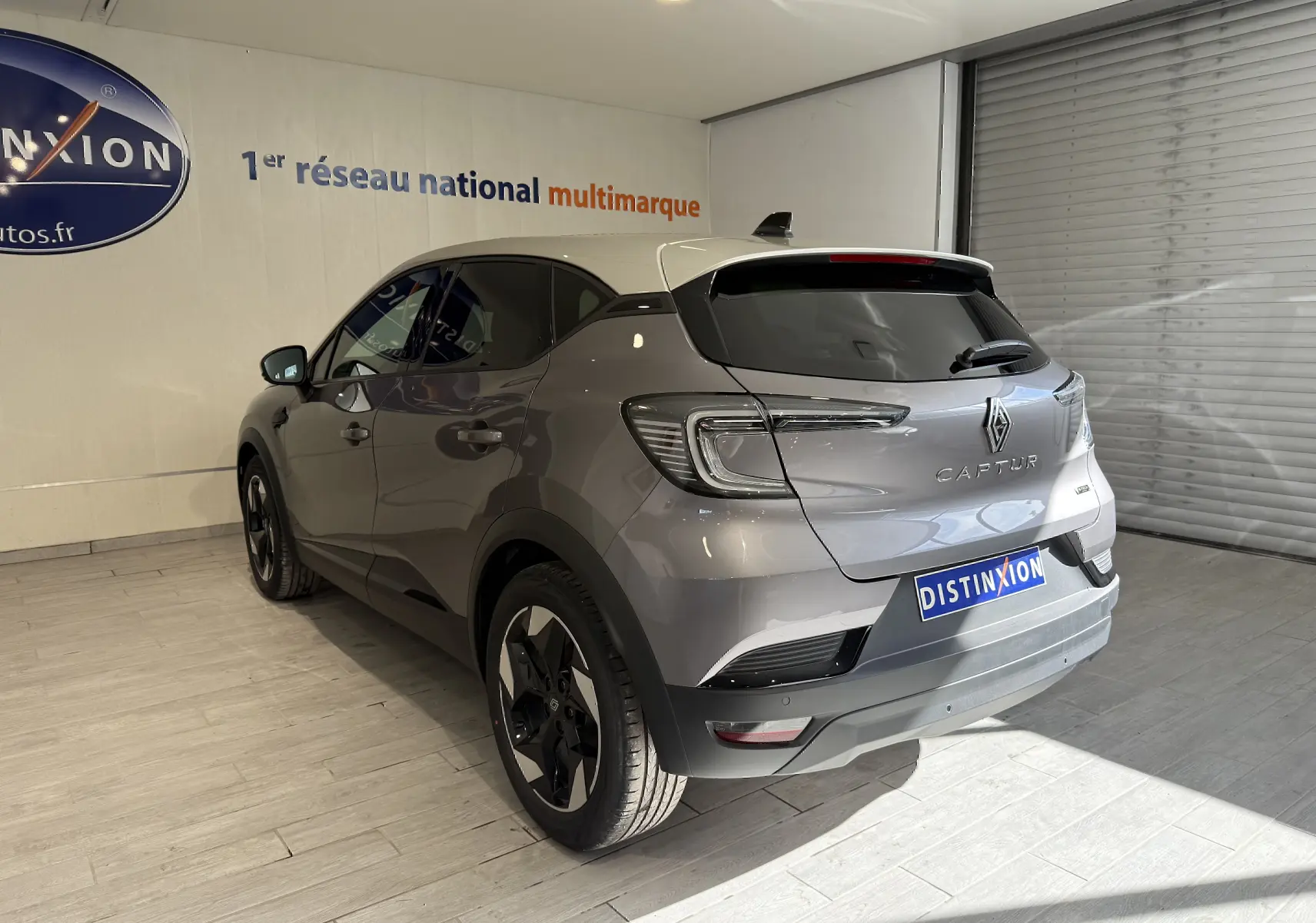 Vue 3/4 arrière droite du Renault Captur 2025 gris Cassiopée métal avec toit gris et jantes noires en showroom.