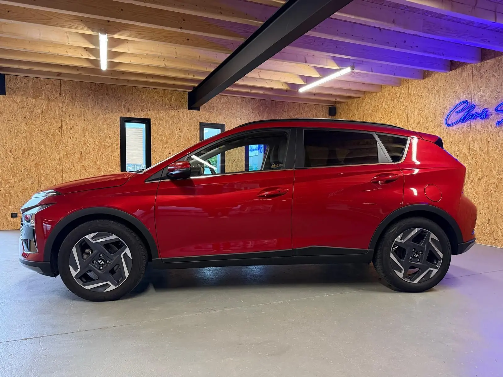 Profil côté gauche du Hyundai Bayon rouge 2025 avec jantes alu 17'' et rétroviseurs électriques dans un garage.