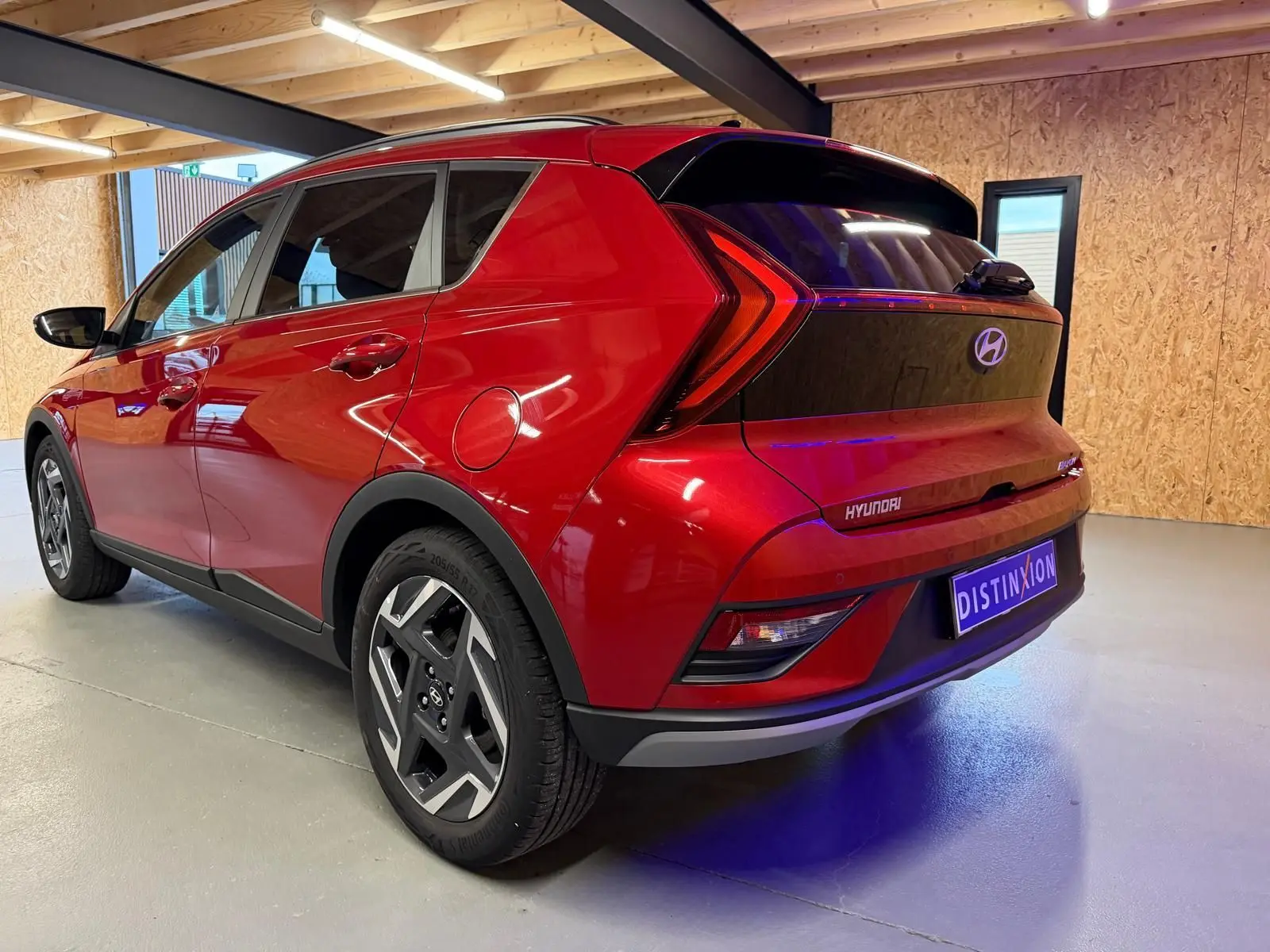 Vue 3/4 arrière droite d'une Hyundai Bayon rouge avec calandre noir laqué et jantes alu 17 pouces dans un garage.