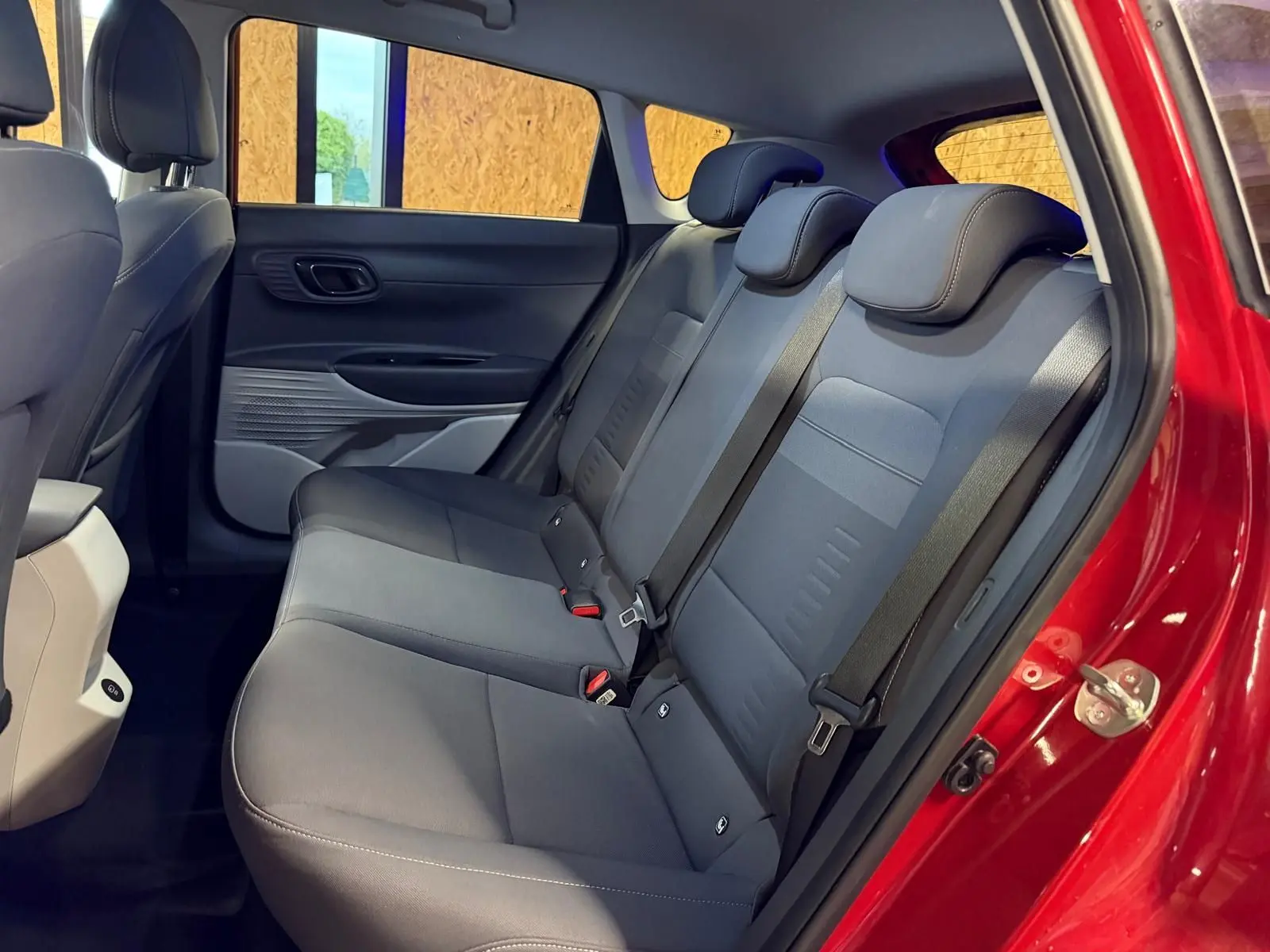 Vue intérieure côté droit sur la banquette arrière grise du Hyundai Bayon rouge avec ceinture de sécurité visible.