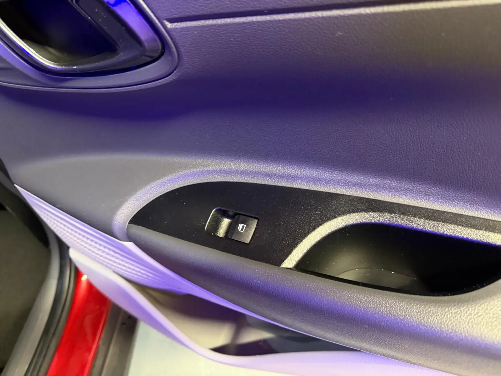 Gros plan sur la commande de lève-vitre côté conducteur d'une Hyundai Bayon rouge, intérieur noir.