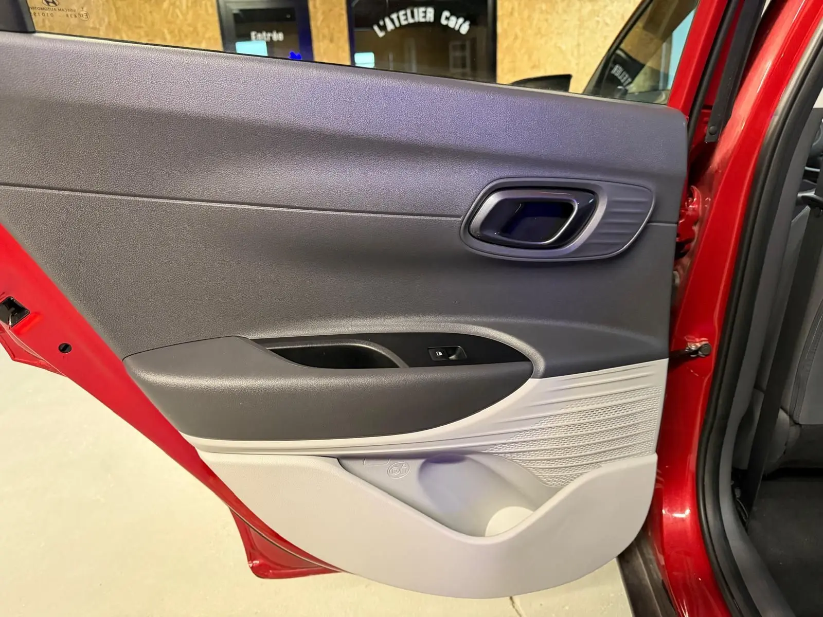 Porte arrière côté gauche ouverte d'une Hyundai Bayon rouge, intérieur bi-ton noir et gris clair avec poignée chromée.