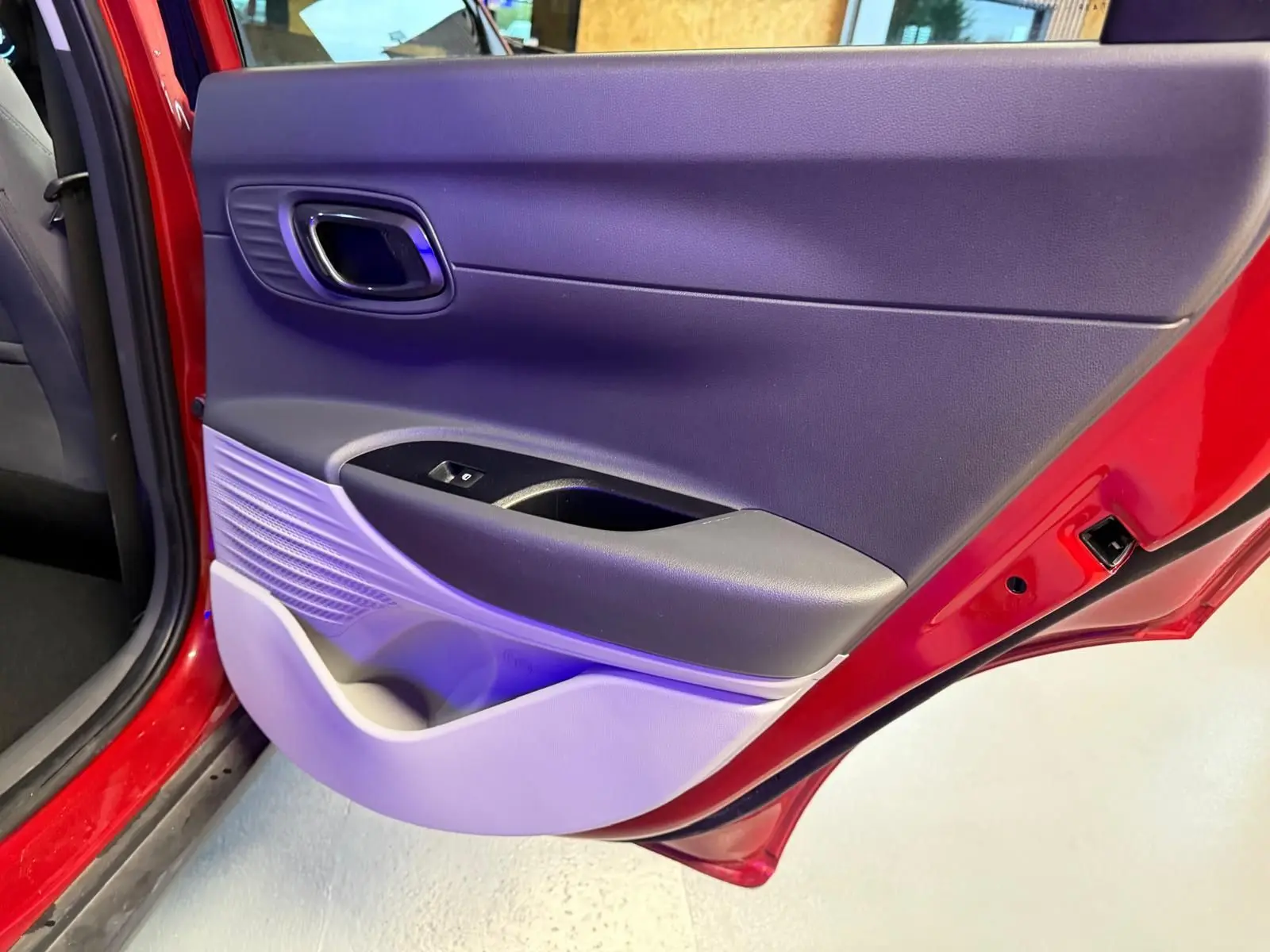 Vue rapprochée de la porte arrière gauche rouge d'une Hyundai Bayon avec panneau intérieur noir et gris clair.