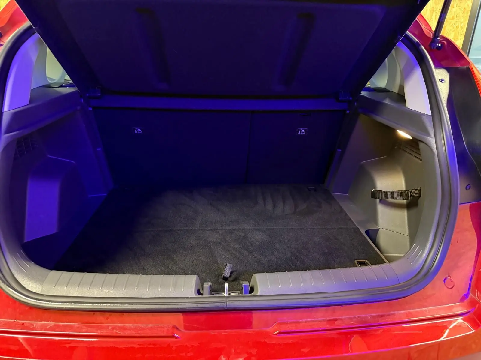 Coffre ouvert vu de l'arrière d'une Hyundai Bayon rouge 2025, espace de chargement propre et éclairé.