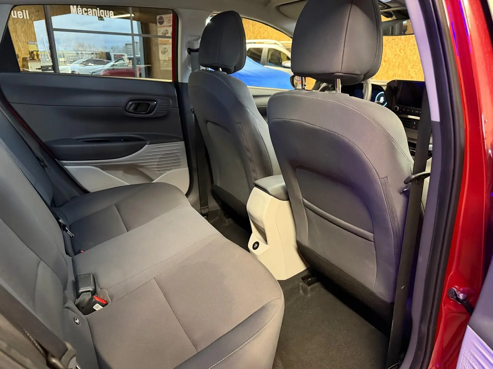 Vue arrière côté gauche de l'intérieur du Hyundai Bayon rouge 2025, sièges tissu gris et console centrale beige.