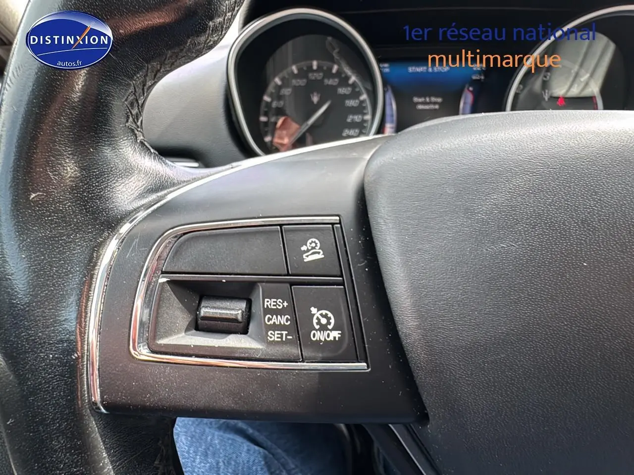 Gros plan sur les commandes de régulateur de vitesse au volant cuir noir d’un Maserati Levante gris.